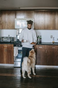 A man enjoys a quiet morning with coffee and a dog in his kitchen.